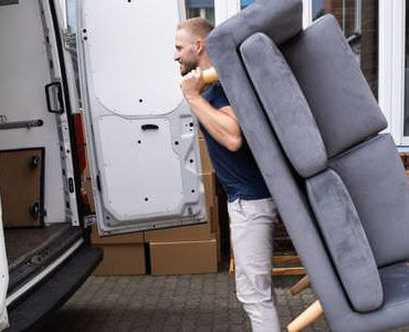 Möbellift Cottbus: Helfer tragen ein graues Sofa aus einem Transporter